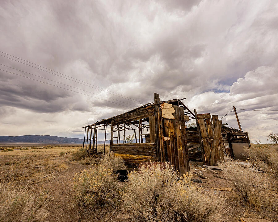An abandoned wooden building beneath dramatic clouds in a barren landscape.
