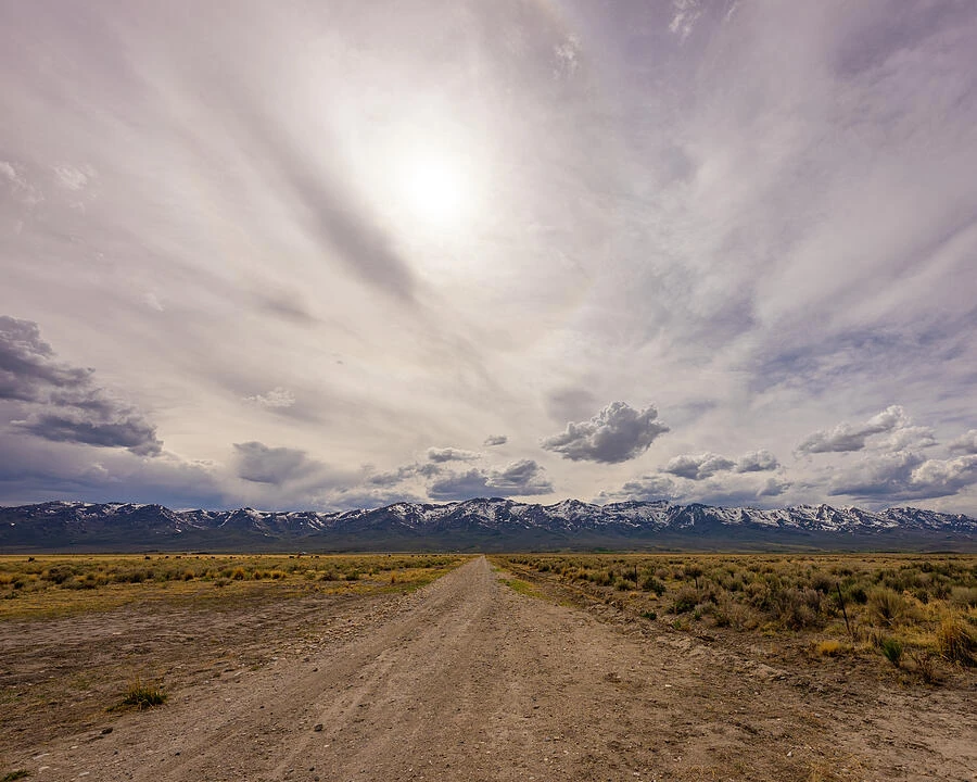 A gravel road leads toward distant mountains beneath a wide, cloudy sky.
