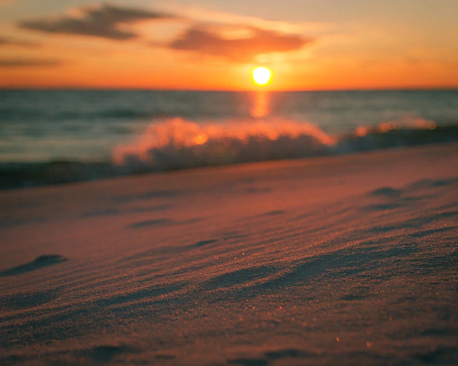 Golden sunset light across rippled sand and waves breaking along the shore.