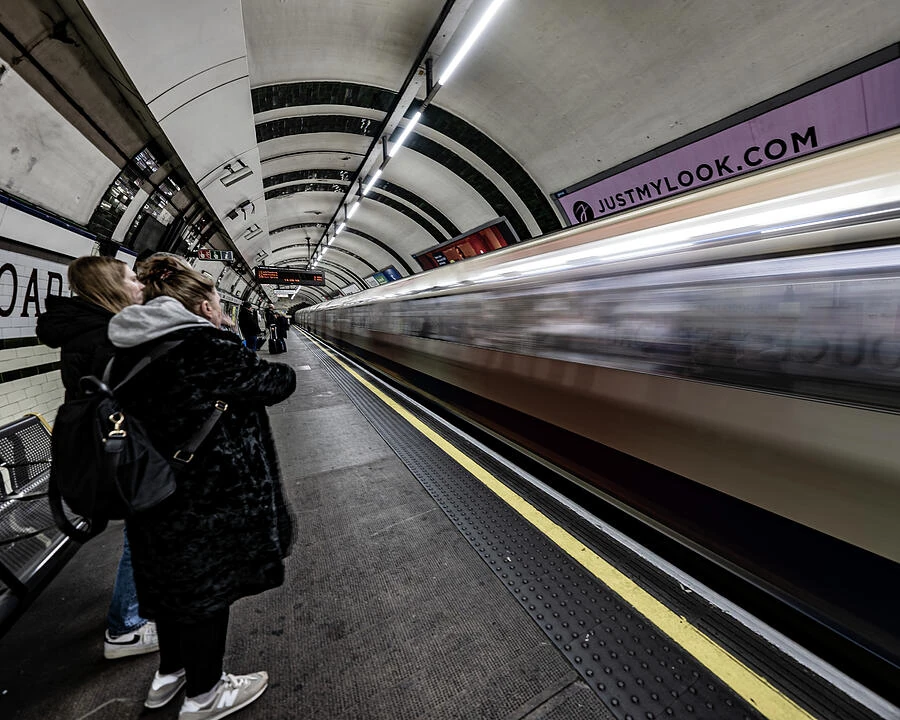 A moving London Underground train blurs past passengers waiting on the platform.
